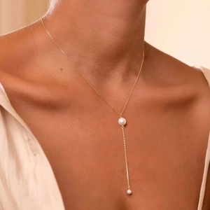 Detailed view of the gold Y-lariat necklace with two white freshwater pearls on a model