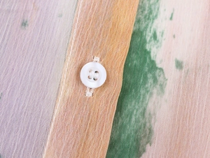 Vue macro d'un bouton blanc et d'un imprimé aquarelle coloré sur un tissu léger et doux