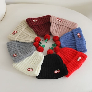 Close-up of thick ribbed knit fabric and cherry embroidery on children's winter beanies