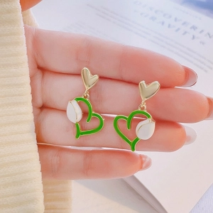 Detailed view of green tulip heart earrings held between fingers for size reference