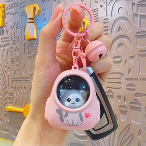 Cute pink cat space capsule keychain with bell held by hand against a grey wall