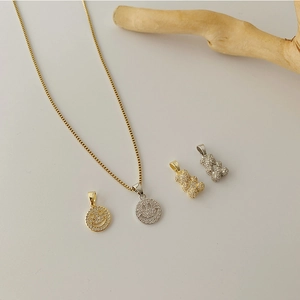 Detailed view of micro-paved zircon bear and smiley face pendants on gold cross chain