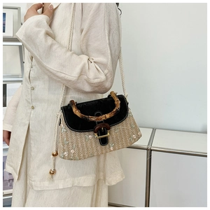 Detail of hand-woven straw bag featuring a bamboo handle and contrast black PU leather flap