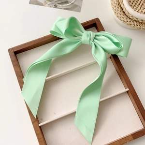 Detail of mint green satin bow hair clip with long ribbons on a wooden display tray