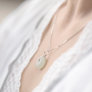 Close-up of a silver necklace featuring a wire-wrapped light green gemstone pendant on model