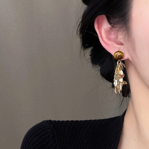 Close-up of golden leaf tassel earrings with brown resin bead on a model ear