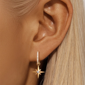 Close-up of gold starburst earrings with zircon worn by a model in a natural setting