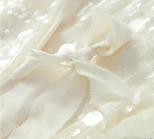 Detailed view of sequin stitching and soft fabric ribbon bow on a white blouse