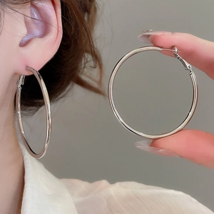 Close-up of large silver hoop earrings worn to show size and smooth metallic finish
