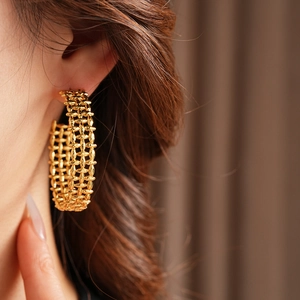 Close-up of gold woven mesh C-shape hoop earring worn by a model with warm lighting