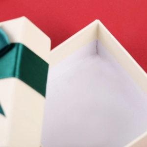 Square beige gift box with deep green ribbon and white interior on red background