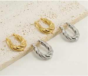 Macro detail of twisted 18K gold and silver U-shaped hoop earrings on stone