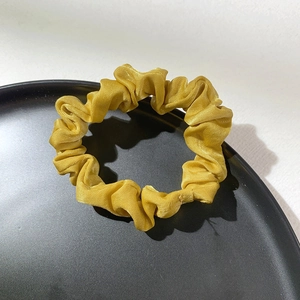 Detail of yellow satin hair scrunchie with pleated texture on a black aesthetic tray