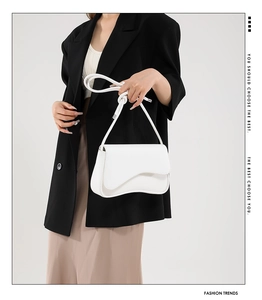 White shoulder bag featuring curved flap design and knotted strap detail worn by model
