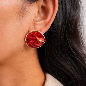 Close-up of a large red round earring featuring irregular texture and enamel finish