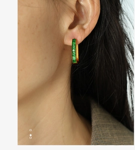 Detail of gold rectangular green zircon hoop earring on a model in a plaid blazer