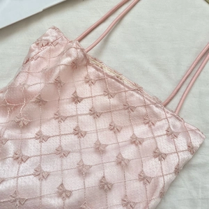 Gros plan du haut en satin rose avec motif matelassé et détails de broderie de nœuds délicats
