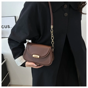 Detail of a brown saddle bag featuring a gold three-ring lock and chain shoulder strap