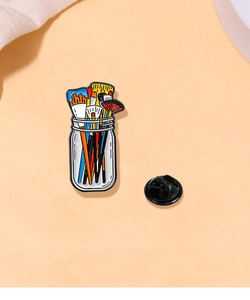 Detail of colorful paintbrush jar enamel pin with black rubber clutch back on warm background