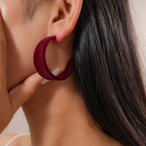 Close-up of deep red velvet geometric C-shaped earring worn by a model in soft light