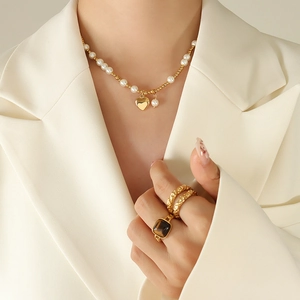 Beaded pearl necklace with gold heart pendant and tiger eye stone ring on a model