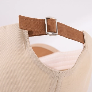 Detail of adjustable metal buckle and brown fabric strap on the beige cotton baseball cap