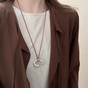 Macro shot of an irregular C-shaped metallic pendant on a dark brown leather cord