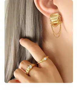 Close-up of gold fringe chain earrings and textured rings on model with warm lighting