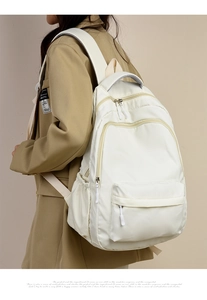 Side view of a creamy white nylon backpack on a model showing side pockets and zippers