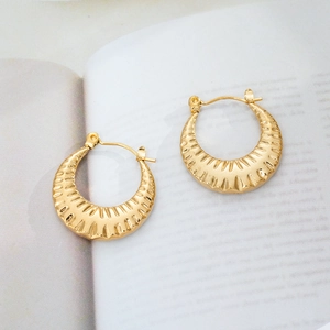 Detail of 18K gold plated hoop earrings with textured vertical ridges on an open book