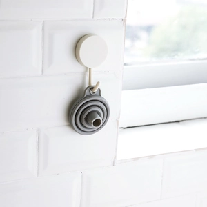 Space-saving grey silicone foldable funnel hanging on a hook against white tiles