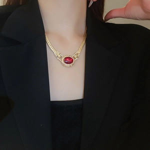 Close-up of vintage gold necklace with oval red ruby pendant on a model in a black suit
