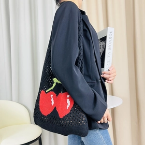 Detail view of a black crochet tote bag featuring large red cherry patterns and mesh weave