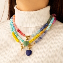 Close-up of layered heart pendant necklace with colorful macaron beads on white sweater