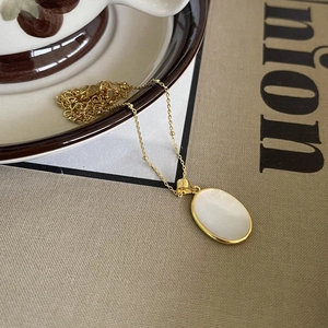Detailed close-up of 925 sterling silver gold necklace with oval shell pendant on a magazine