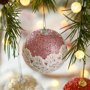 Pink lace Christmas ball ornament with glitter hanging on a festive tree branch