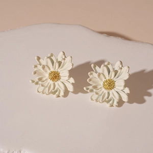 Macro detail of white floral daisy earrings with gold stamen on a white stone base