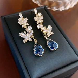 Macro shot of gold drop earrings featuring blue teardrop gems and zircon butterflies