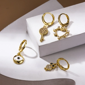 Golden hoop earrings set with crystal key, heart, eye and owl charms on white pedestals