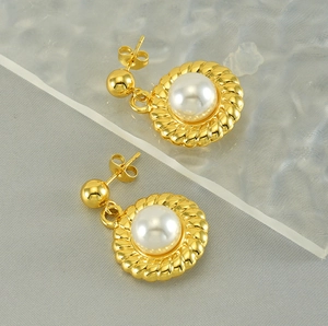 Dettaglio di eleganti orecchini dorati con perla centrale e bordo a corda intrecciata