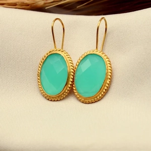 Detail of oval mint green crystal earrings with gold rope edge on white knit fabric