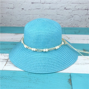 Detail of blue straw sun hat with decorative white beads on blue wooden background