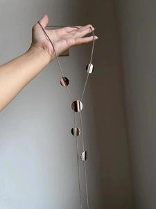 Detailed view of a long Y-shaped necklace with five flat circular metallic charms
