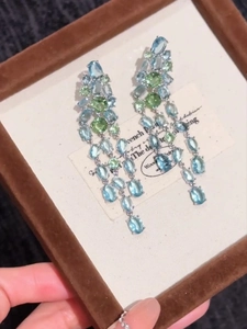Macro view of long tassel earrings with light blue and green crystals in a display box