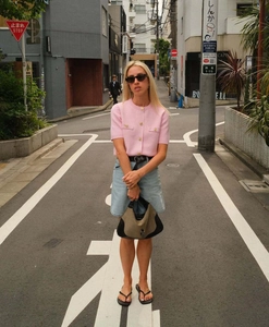 Dettaglio di un cardigan rosa a maniche corte in maglia con bottoni dorati e pantaloncini denim