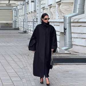 Detail of oversized black long trench coat with stand collar in street style fashion