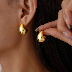 Detail view of golden waterdrop C-shaped stud earrings on a model showing metallic texture