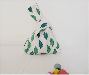 Close-up of cream canvas wristlet knot bag featuring green cartoon tree patterns