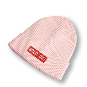 Détail d'un bonnet en maille rose avec un écusson rouge SOLD OUT sur le bord replié