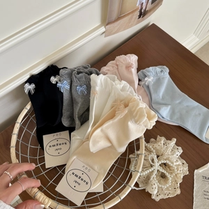 Detail of soft cotton crew socks featuring elegant ribbon bows in a white wire basket